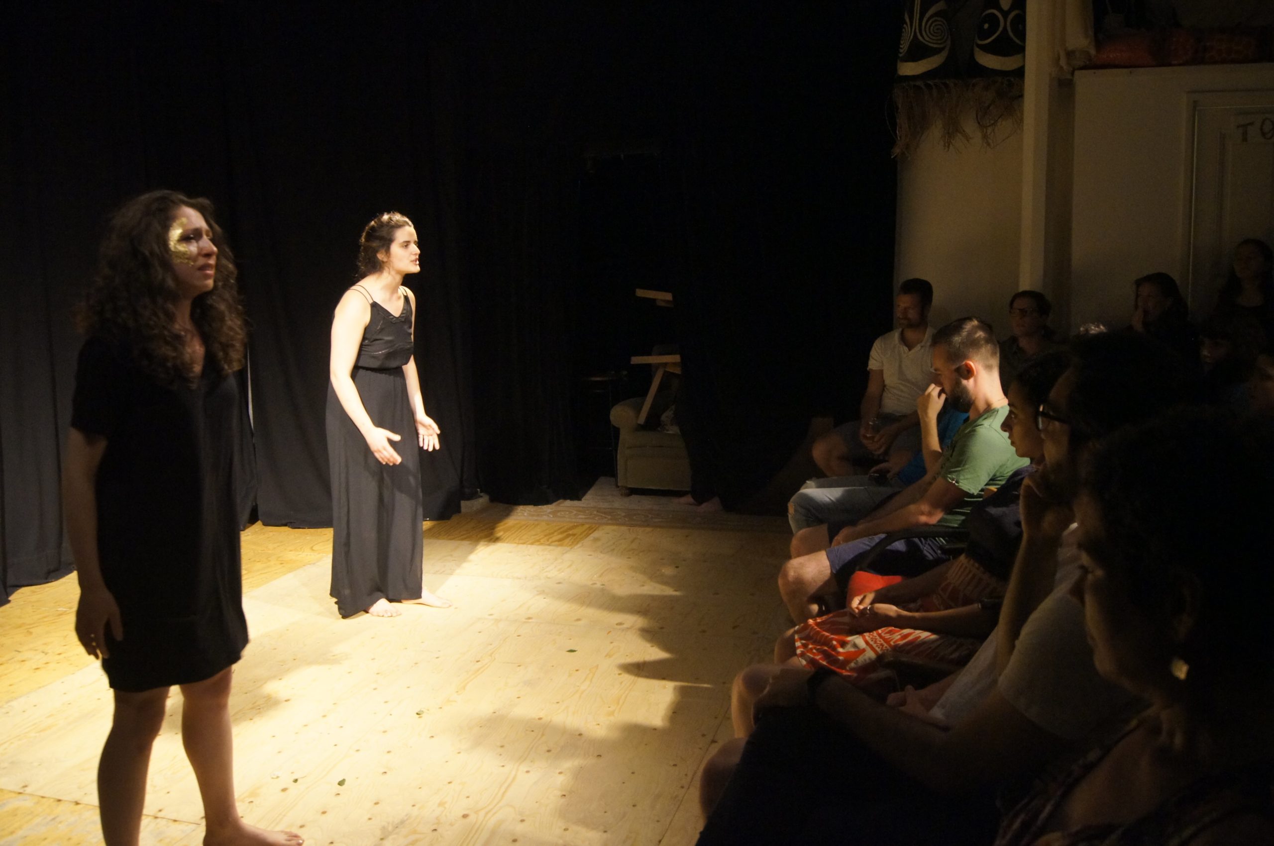 Theatre performance, two women on stage with black dresses, standing in front of audience. They are crying while speaking.