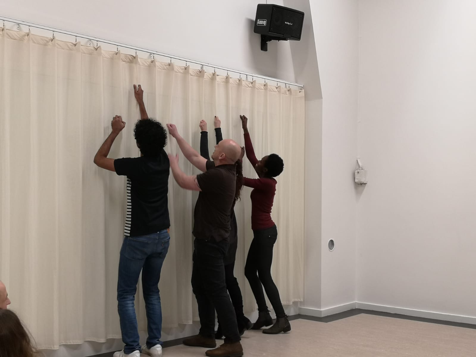 Acting Class Act Attack. A group of four people stand in a row, facing a curtain. Their arms reach up, like they want to bring down the curtain.