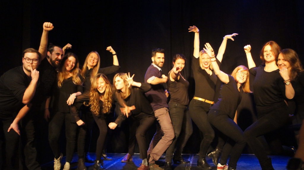 Act Attack's improv and physical show. A group of people on stage wearing black clothes. Group photo after the show, everybody picks a different pose