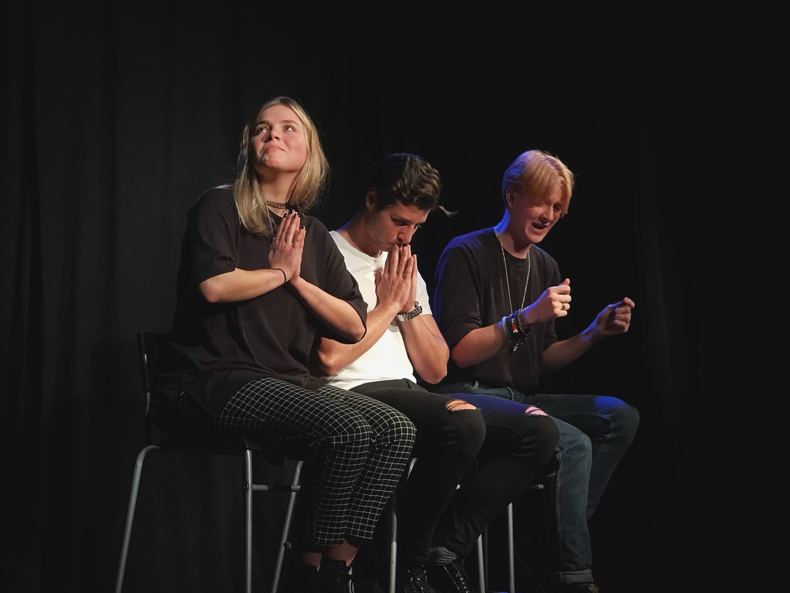 Act Attack's Pure Improv show. Two guys and a girl sit on bar stools. One of them pretends to drive, the other two have their palms facing each other in front of their chest
