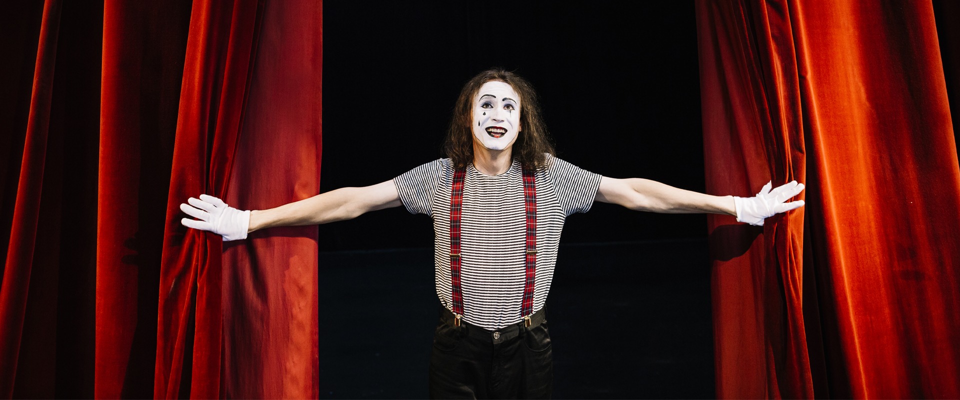Actor masked as Pierrot open the red curtains and enters the stage